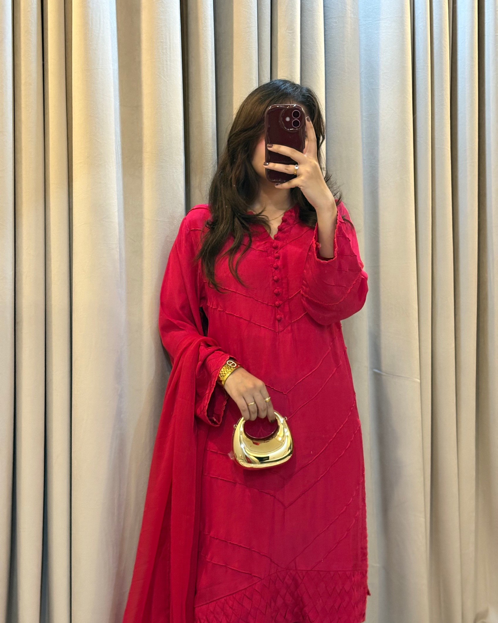 Person wearing a red outfit with a gold handbag against a beige curtain background