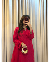 Person wearing a red outfit with a gold clutch in front of beige curtains