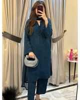 Woman taking a mirror selfie wearing a teal outfit with a patterned handbag indoors.