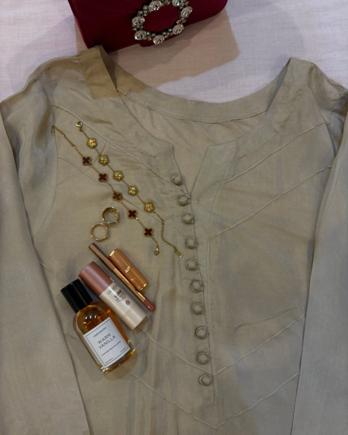 Light-colored blouse with decorative buttons, a necklace, and small bottles on a white background