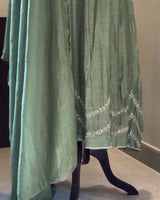 Green dress with white embroidery on a mannequin against a neutral background