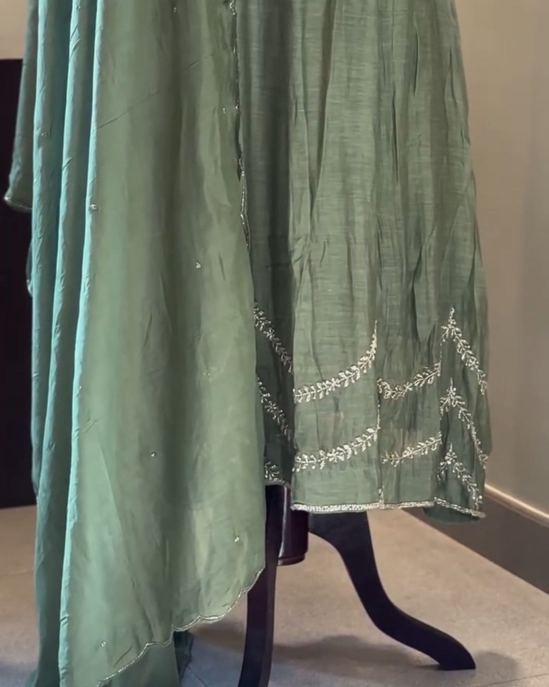 Green dress with white embroidery on a mannequin against a neutral background