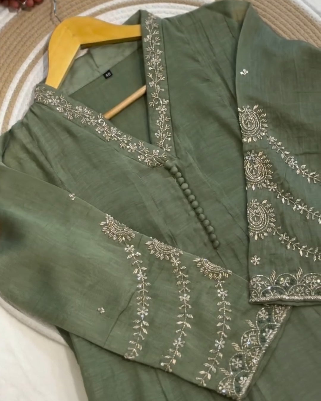 Green embroidered outfit on a hanger against a neutral background