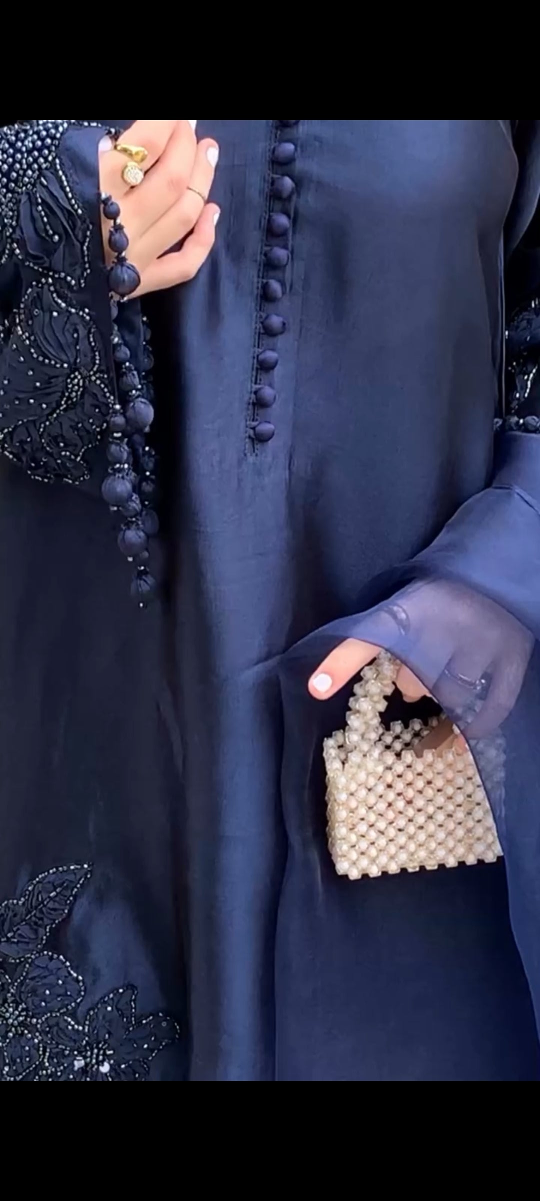 Person wearing a dark blue garment with a beaded handbag