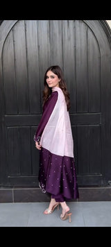 Woman wearing a purple and white traditional outfit against a dark wooden door.