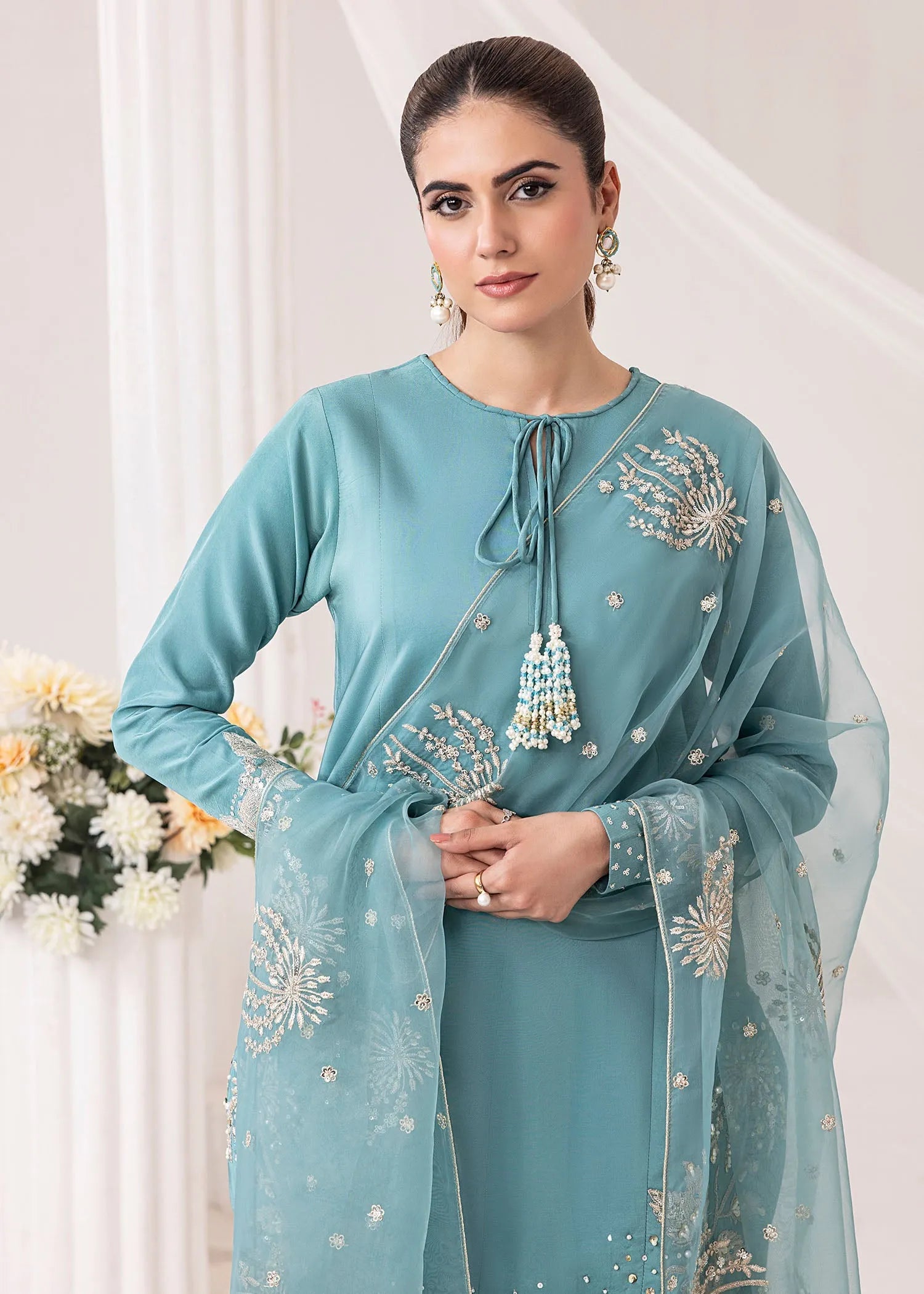 Woman wearing a light blue traditional outfit with floral embroidery in a white setting.