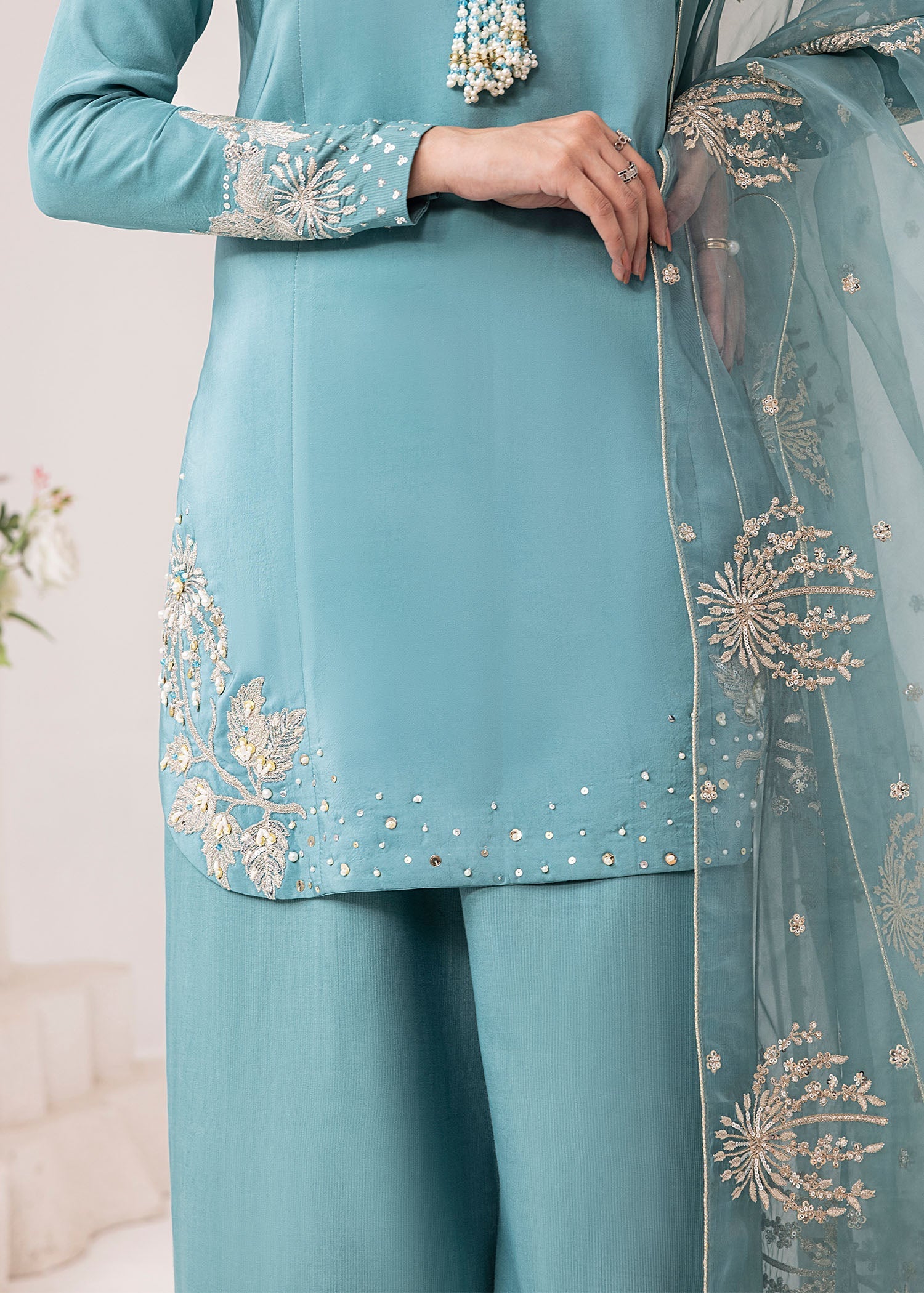 Teal traditional outfit with intricate gold embroidery on a light background