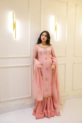 Woman in a pink traditional outfit standing against a white wall with decorative lights.