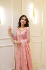 Woman in a pink traditional outfit with gold details against a white wall.