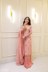 Woman in a pink traditional outfit standing against a white paneled wall.