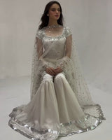 Woman wearing a white embroidered traditional outfit on a plain background