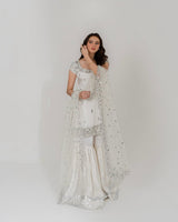 Woman wearing a white traditional outfit with a sheer dupatta against a plain background